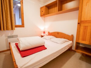 A single bed with white bedding and a red blanket, a bedside table with a lamp, and wooden furniture. - Pleasant apartment pets welcome - 6 guests (Valfréjus)