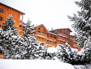 En flerlags bygning af træ med balkoner, omgivet af sneklædte træer.