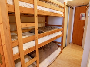 Ein Etagenbett mit drei Schlafstellen, aus Holz, mit einer Tür auf der rechten Seite.
