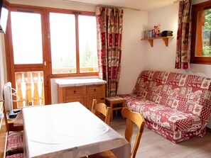 Ein gemütliches Zimmer mit einem Holztisch, einer Couch mit gemustertem Bezug und einem Fenster mit Vorhängen.