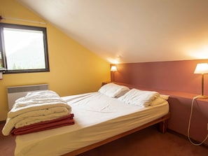 A single bed with a white mattress and pillows, a bedside table with a lamp, a window with a view of trees, and a radiator under the bed. - Spacious apartment, pets welcome - 8 guests (Valfréjus)