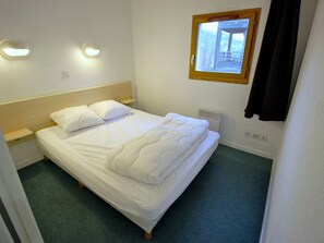 A neatly made bed with pillows, a bedside table, a wall-mounted light, a window with a view, and a thermostat. - Apartment, piste view - 6 guests (Villarodin-Bourget)