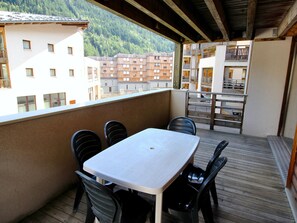 A balcony with a table and chairs, overlooking a mountainous area with buildings. - Apartment, piste view - 6 guests (Villarodin-Bourget)