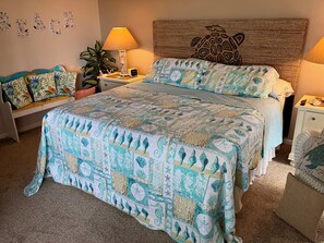 A bedroom with a bed, bedside tables, a lamp, a nightstand, a wall decoration, and a plant. - Enjoy a Slice of Paradise on Ft. Myers Beach! (Fort Myers Beach)
