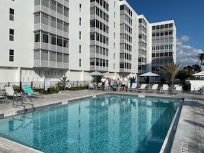A swimming pool with clear blue water, surrounded by lounge chairs and umbrellas, with a multi-story building in the background. - Enjoy a Slice of Paradise on Ft. Myers Beach! (Fort Myers Beach)
