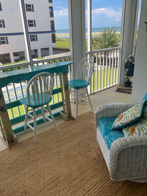 Ein Balkon mit einem Korbsessel und -stühlen, Blick aufs Meer und eine Statue.