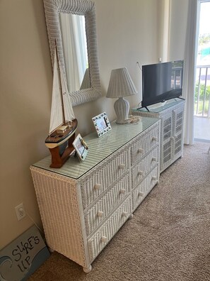 Ein Zimmer mit einer weißen Korbtischkonsole, einem Fernseher, einem Spiegel und einem kleinen Segelbootmodell.