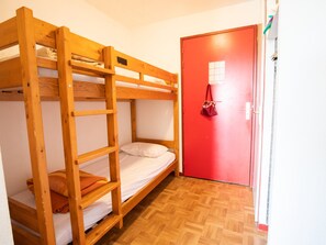 Quarto com beliche, porta vermelha e chão de madeira.