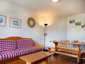 Quarto acolhedor com um banco de madeira, um sofá com manta xadrez e uma mesa de jantar posta para quatro pessoas.