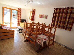 A room with a wooden dining table, chairs, a television, and a window with curtains. - Apartment pets, mountain view - 6 guests (Valfréjus)