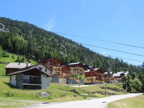 A row of chalet-style buildings with balconies, set against a backdrop of a forested mountain. - Apartment pets, mountain view - 6 guests (Valfréjus)