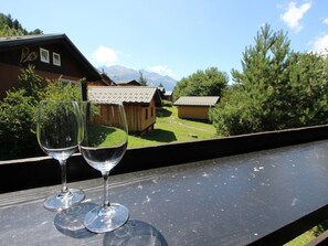 Two empty wine glasses on a balcony with a view of a mountain and wooden buildings. - Chalet with mountain view - 6 guests (Villarodin-Bourget)