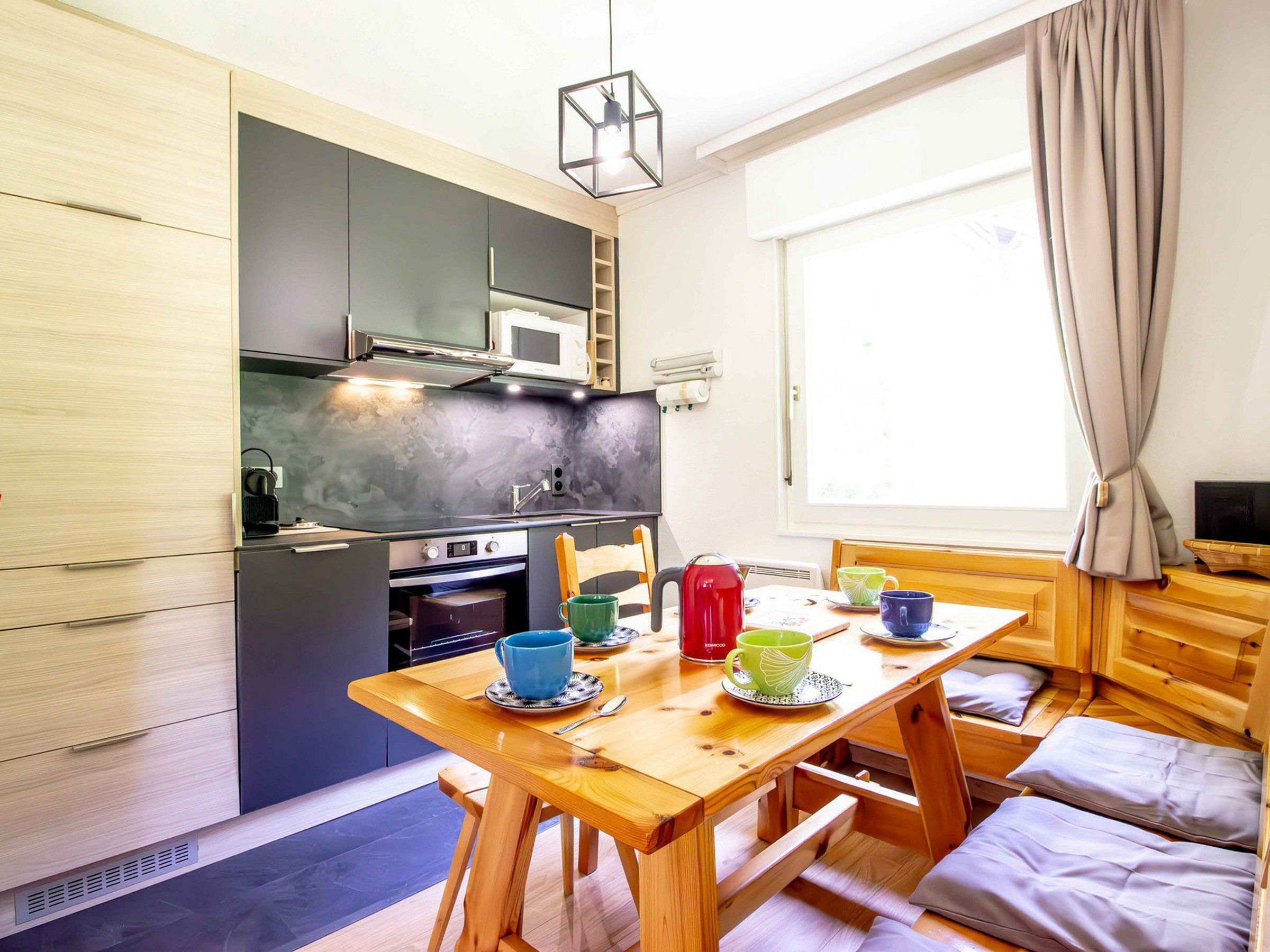 Una cucina compatta con elettrodomestici moderni, un tavolo da pranzo con sedie e una finestra con tende.