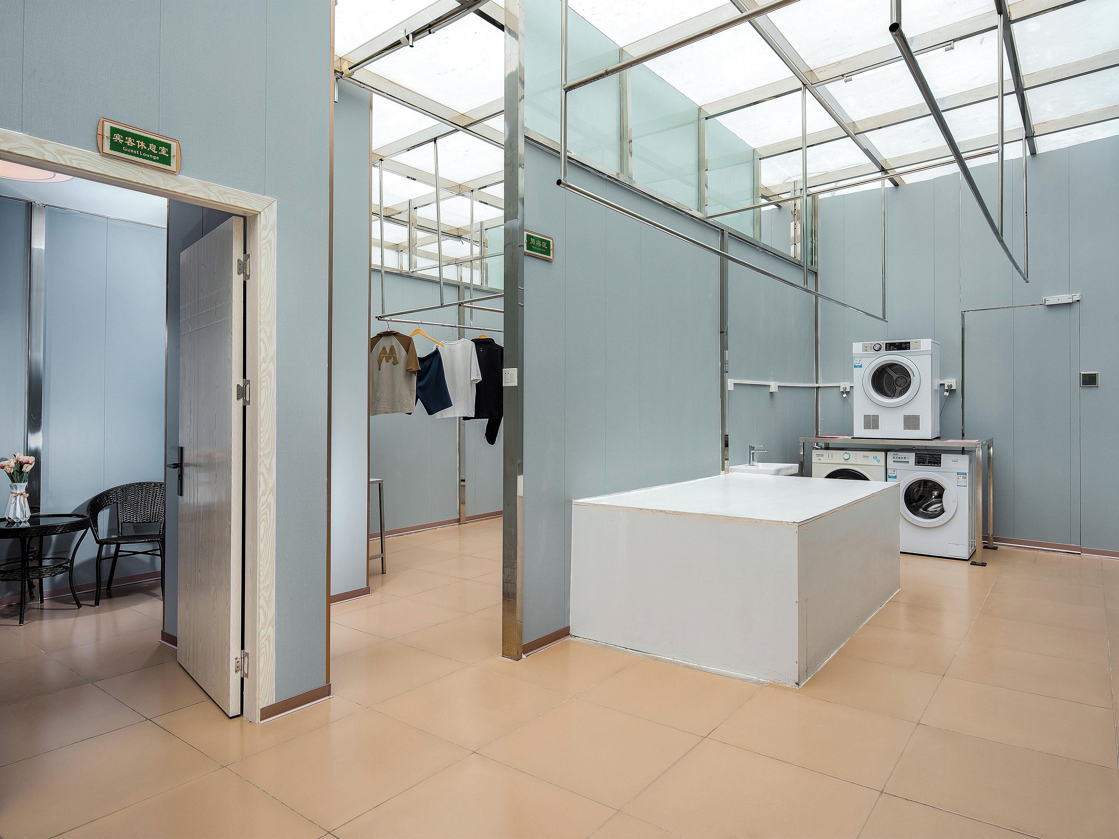 A hotel room with a bed, a desk, a chair, a washing machine, and a mirror.