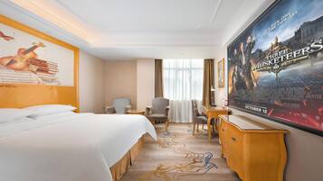 Une chambre d’hôtel avec un lit, deux fauteuils, un bureau, une grande affiche et une fenêtre avec des rideaux.