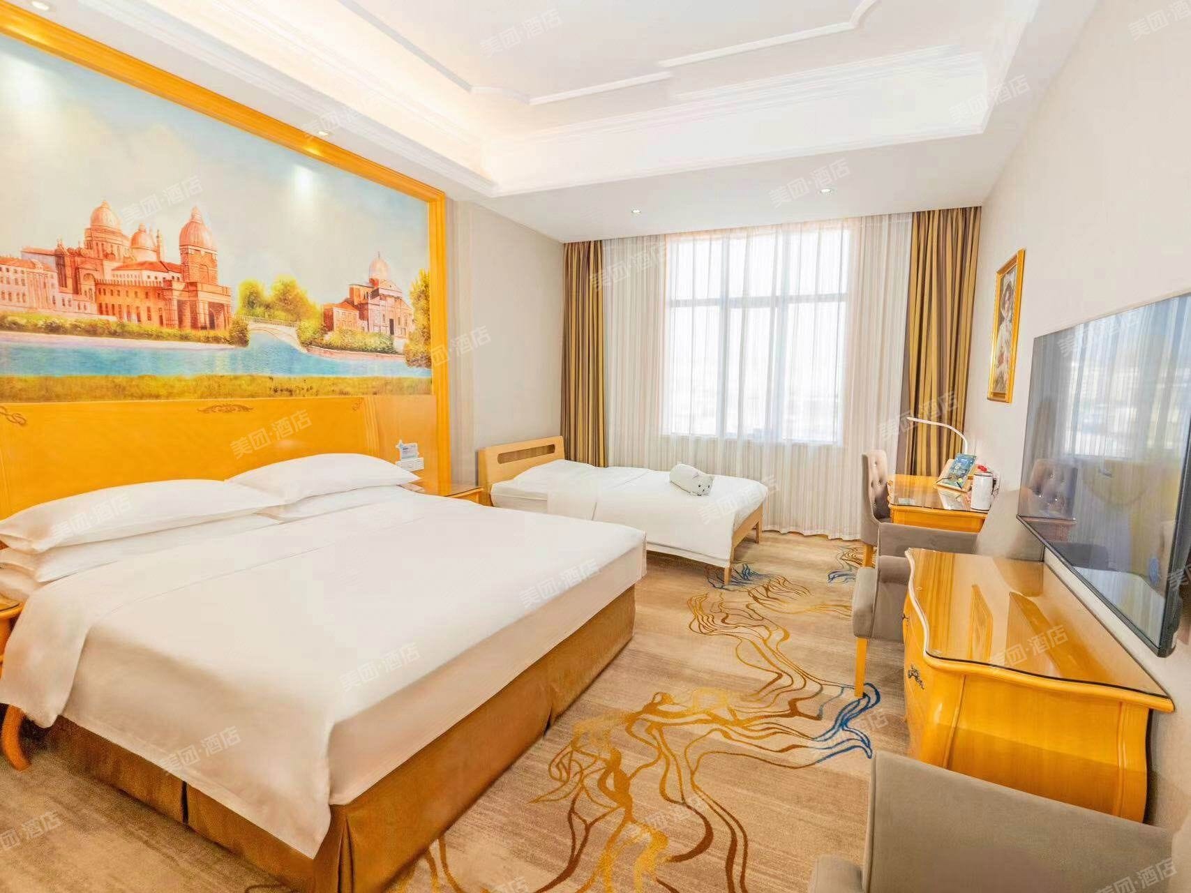 A hotel room with two beds, a desk, a television, and a large painting on the wall.