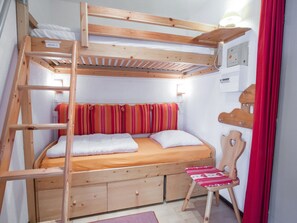 Un llit superposat amb una escala, una petita cadira de fusta i una prestatgeria penjada a la paret.