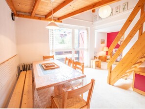 A dining area with a wooden table, chairs, a hanging light fixture, and a view through a window. - Spacious apartment at the foot of the slopes - 8 guests (Villarodin-Bourget)