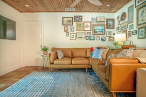 Ein Wohnzimmer mit einem braunen Ledersofa, einem blau gemusterten Teppich und einer Wand, die mit verschiedenen gerahmten Kunstwerken geschmückt ist.