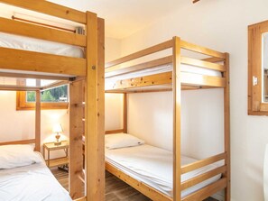 Ein Zimmer mit zwei Etagenbetten, einem Nachttisch mit Lampe und einem Fenster mit Blick ins Grüne.