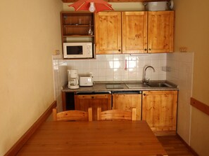 A compact kitchen with wooden cabinets, a microwave, a coffee maker, and a sink. - Cozy apartment at the foot of the slopes - 4 guests (Valfréjus)