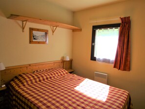 A room with a bed, a window with curtains, a wall-mounted picture, and a wooden shelf. - Cozy apartment at the foot of the slopes - 4 guests (Valfréjus)