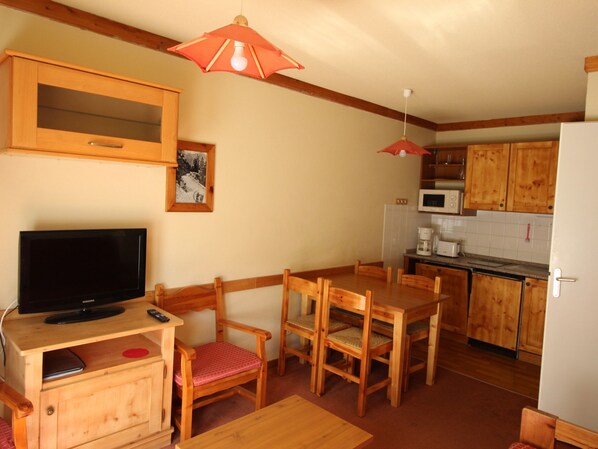 A compact kitchen with wooden cabinets, a microwave, a refrigerator, a dining table with chairs, and a television on a wooden stand. - Cozy apartment at the foot of the slopes - 4 guests (Valfréjus)