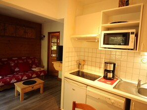 A compact kitchen with a microwave, stove, and sink. There's a wooden table and a sofa in the adjacent living area. - Cozy and quiet studio - 4 guests (Villarodin-Bourget)