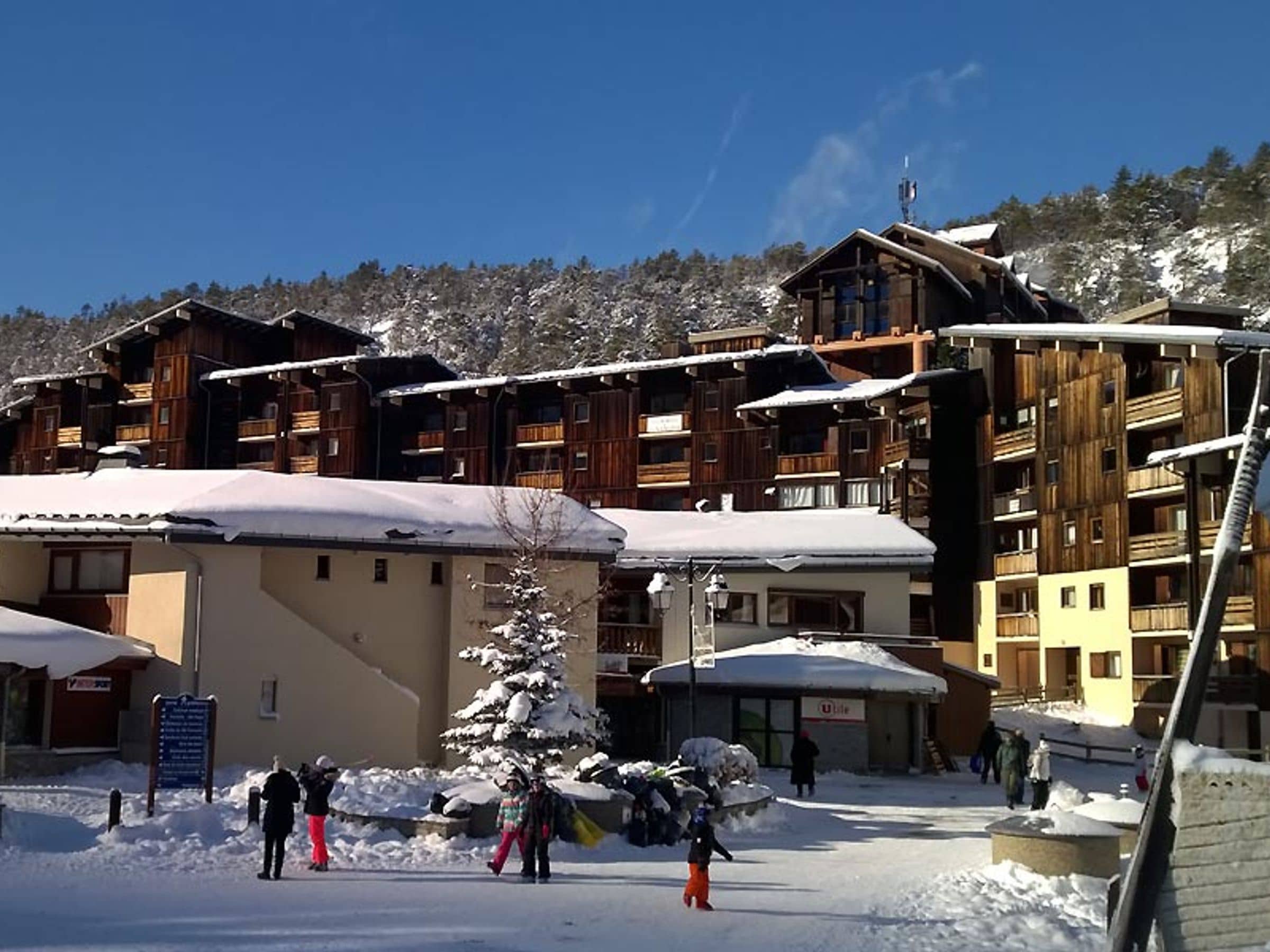 A ski resort with wooden buildings, a covered parking area, and a snow-covered tree.