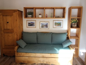 Ein Holzsofa mit gemusterten Kissen, ein Holzkabinett und Regale mit Dekoration und gerahmten Bildern.