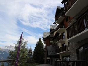 A multi-story building with balconies, a mountain view, and a clear sky. - Apartment at the foot of the slopes - 4 guests (Valfréjus)
