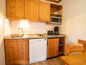 Ett kompakt kök med träskåp, en inbyggd mikrovågsugn, en diskmaskin och en kaffebryggare.