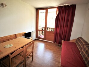 A room with a wooden table, chairs, a bed with a plaid cover, a television, and a window with curtains. - Studio in village center, at the foot of slopes - 3 guests (Valfréjus)