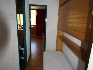 En smal gang med en seng til højre og en dør, der fører til et andet værelse.