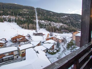 Un pueblo nevado en la montaña, con edificios, una pista de esquí y una colina arbolada.