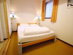 A single bed with a wooden frame, two bedside lamps, and a window with curtains. - Quiet apartment by the forest - 4 guests (Villarodin-Bourget)