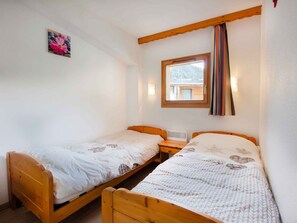 Ein Zimmer mit zwei Holzbetten, einem Vorhangfenster und einem an der Wand hängenden Bild.