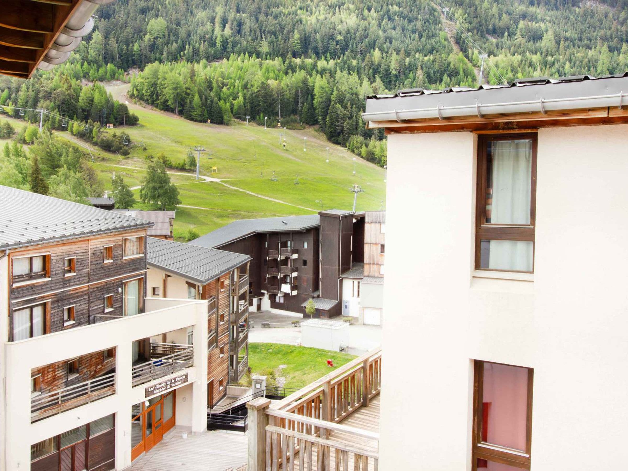 A multi-story building with balconies, a ski lift in the background, and a mountainous landscape.