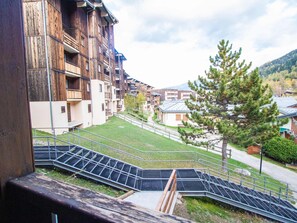 A residential building with a wooden facade, a grassy courtyard, and a staircase leading to a pedestrian path. - Comfortable studio with balcony - 4 guests (Villarodin-Bourget)