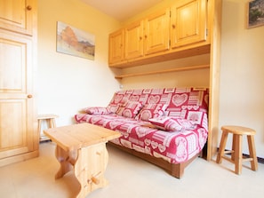 A cozy room with a wooden sofa, a small wooden table, and a wooden stool. - Comfortable studio with balcony - 4 guests (Villarodin-Bourget)