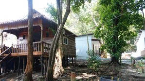 A wooden house with a balcony, surrounded by trees and a garden area.
