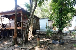 A wooden house with a balcony, surrounded by trees and a garden area.
