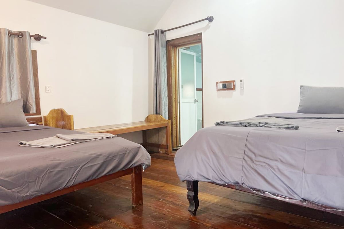 A room with two beds, a wooden bench, a small table, and a door leading to another room.