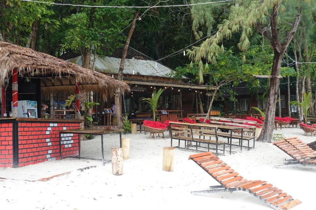 Um restaurante à beira-mar com área externa, estrutura de palha e piso de areia.