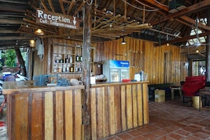 A rustic reception area with wooden walls, a counter, and a refrigerator. - Rock Sand Hostel (Koh Rong)