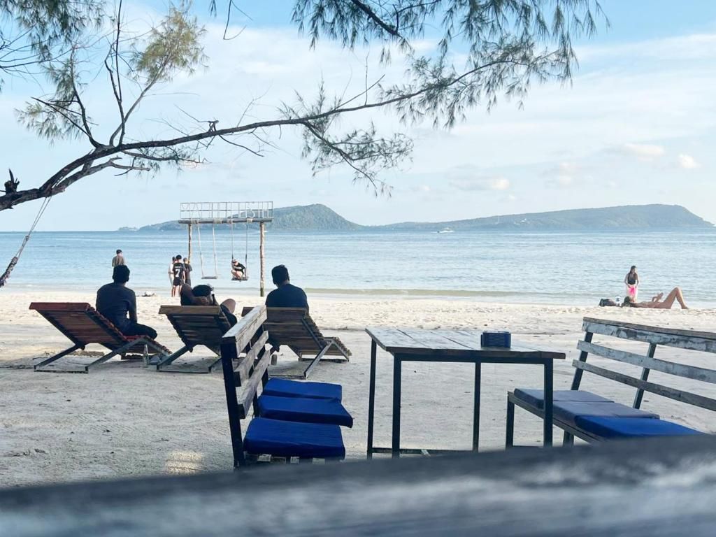 Uma praia com espreguiçadeiras e uma mesa, céu claro e mar calmo.
