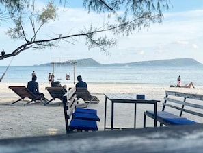 A beach with sun loungers and a table, a clear sky, and a calm sea. - Rock Sand Hostel (Koh Rong)