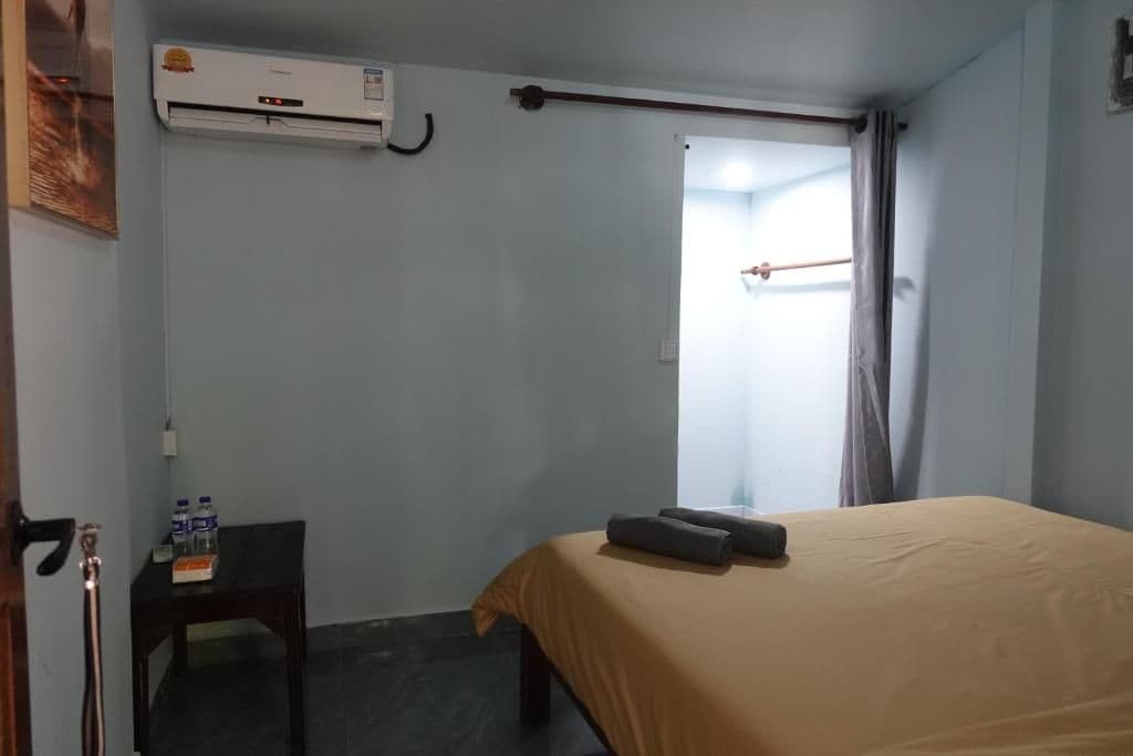 A hotel room with a bed, an air conditioning unit, a small table with bottled water, and a door leading to another room.