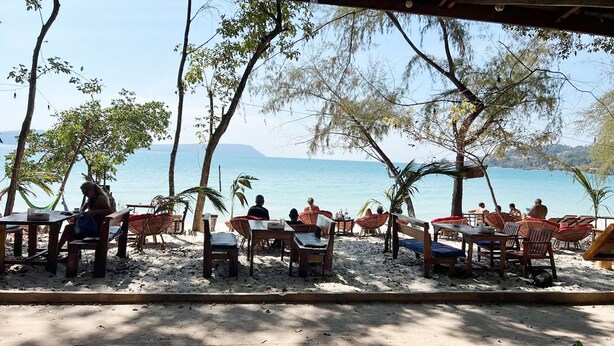 An outdoor seating area with tables and chairs, overlooking a body of water. - Rock Sand Hostel (Koh Rong)