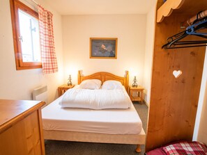 Ein Schlafzimmer mit einem Bett, zwei Nachttischen, einem Fenster mit Vorhängen, einem Bild an der Wand und einem Holzschrank mit Herz-Aussparung.